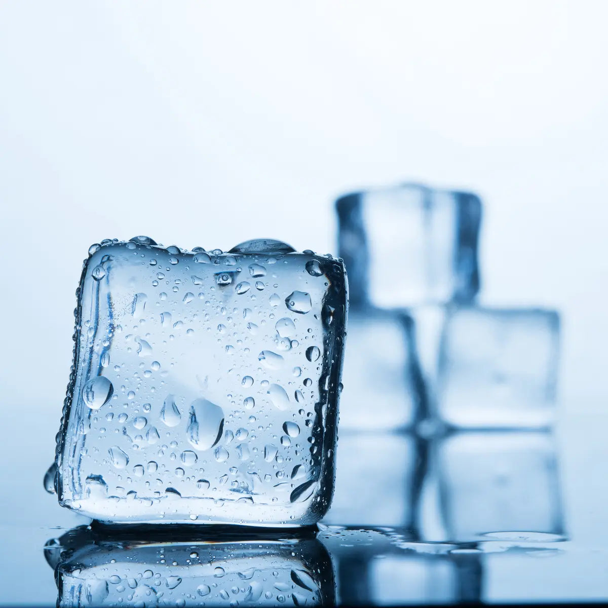 Close-up of fresh ice cubes with water droplets on a reflective surface, set against a cool blue background, symbolizing cold and refreshing purity.